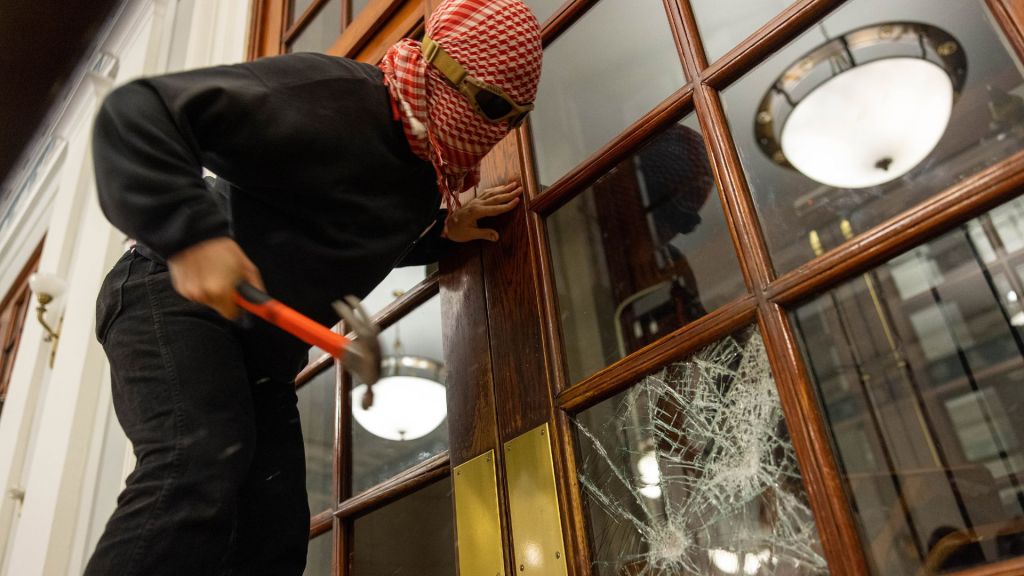 Üniversiteli bir protestocu Hamilton Hall'un ön kapısının etrafına zincir çekerek yetkililerin içeri girmesini engellemek üzere kapının camlarını kırıyor. Columbia Üniversitesi, New York, 30 Nisan 2024. Fotoğraf: Alex Kent, Getty Images.